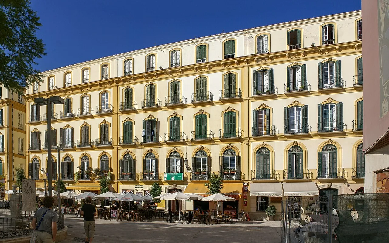 A sunlit square in the historic centre of Málaga with café awnings beneath a nineteenth-century façade